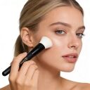 A woman is using a flat-top foundation brush.