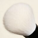 A foundation brush with soft white bristles and a black metal ferrule, placed against a beige background.