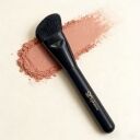 Sophienia angled makeup brush with black handle lying on scattered pink blush powder against cream background