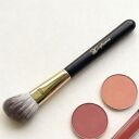 Sophieria makeup brush with black handle and gold ferrule next to two round blush compacts in pink and mauve shades