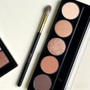 Eyeshadow palette with five neutral shades from matte to glitter, makeup blending brush, and partial palette on white back...