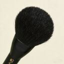 Black powder makeup brush with soft rounded bristles and dark handle against cream background