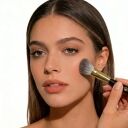 Woman applying blush to her cheek with a Sophienia makeup brush, featuring natural makeup and straight brown hair