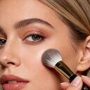 A woman is using a powder brush with snow fox hair.