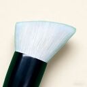 Flat top kabuki makeup brush with soft white bristles and dark green handle against cream background