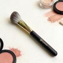 Sophienia makeup brush with black handle and gold ferrule surrounded by pink blush compacts and loose powder