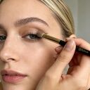 Woman applying eyeshadow with Sophenia makeup brush to eyelid, demonstrating natural eye makeup application technique