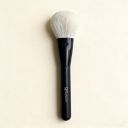 Sophienia makeup powder brush with soft white bristles and sleek black handle on cream background