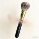 Sophienia powder makeup brush with fluffy gray bristles, gold ferrule, and black handle surrounded by loose powder dust