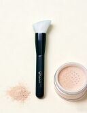Sophienia makeup brush with angled white bristles and dark handle next to open jar of loose setting powder on beige backgr...