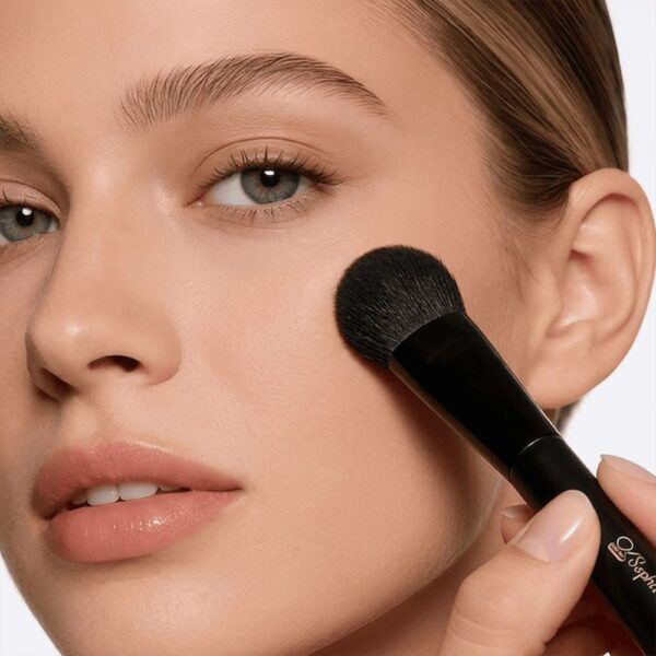 Woman applying blush to cheek with black Sophienia makeup brush, natural makeup look with glossy lips